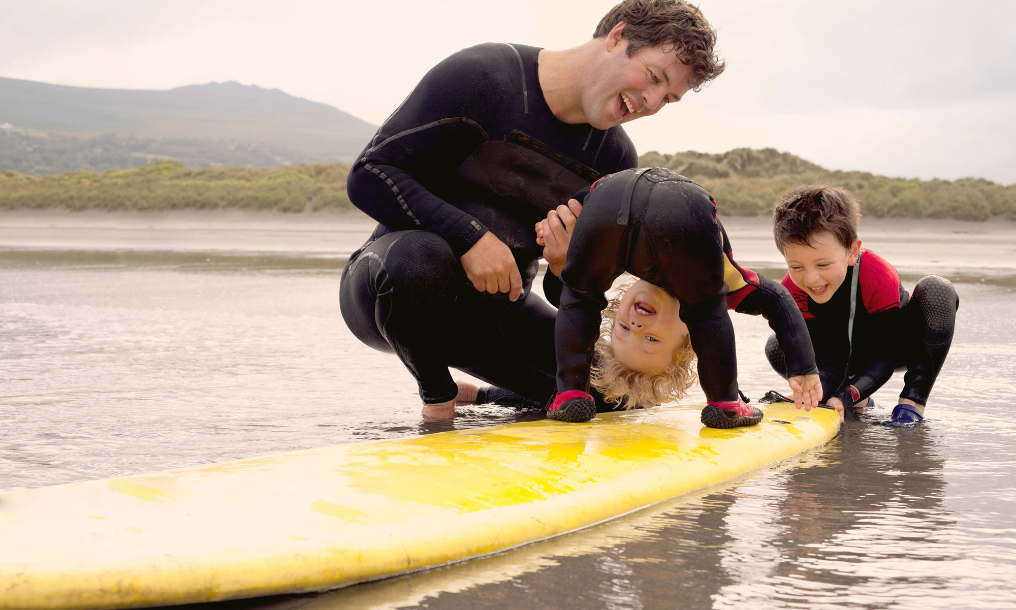 Far med två söner leker på en surfingbräda ute i vattnet